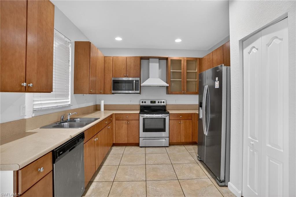 Kitchen featuring wood-finish cabinetry, stainless steel appliances, a dual basin sink, and tile flooring