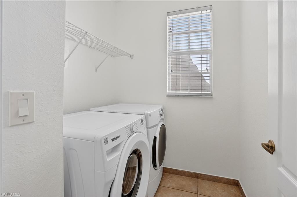 Laundry area featuring a window with horizontal blinds, overhead wire shelving, and tiled flooring