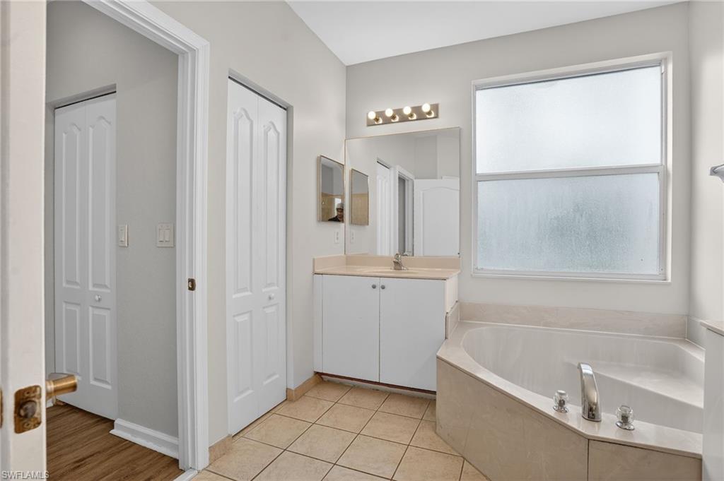 Bathroom featuring a corner soaking tub with deck-mounted fixtures, a single vanity with base cabinetry, and a mirrored medicine cabinet