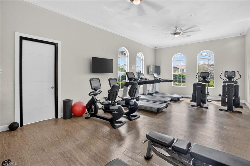 Fitness room featuring wood-finish flooring, three arched windows, two ceiling fans, and two wall-mounted televisions