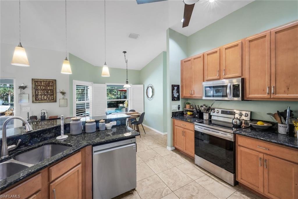 Kitchen featuring wood cabinetry, stainless steel appliances, dark stone countertops, and tile flooring