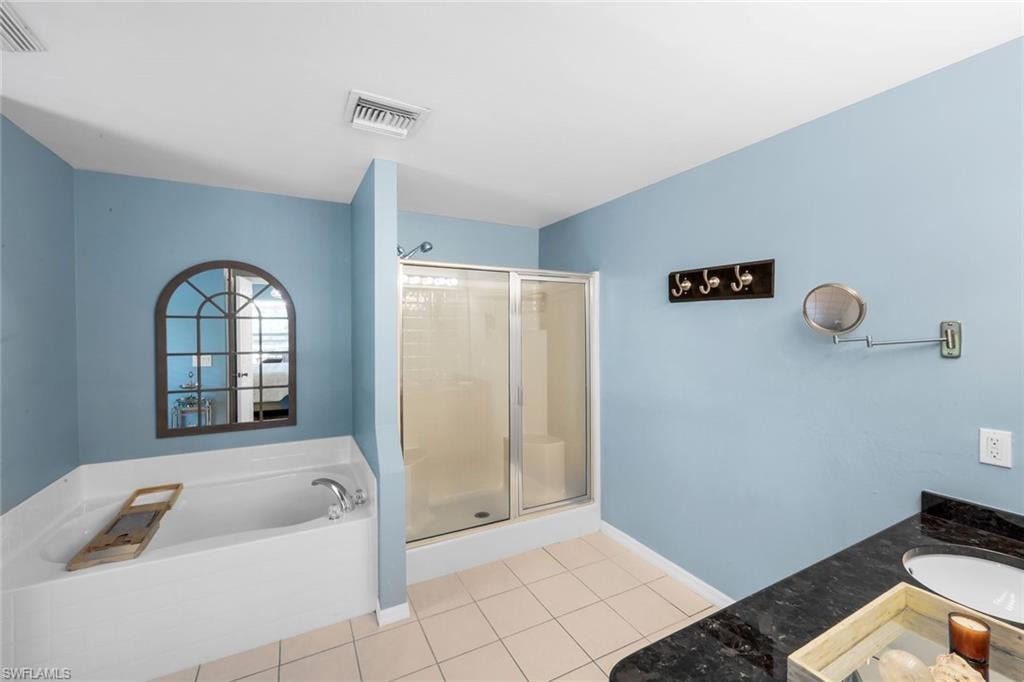 Spacious bathroom featuring an integrated soaking tub, a separate glass-enclosed shower, a vanity with a dark countertop, and tiled flooring
