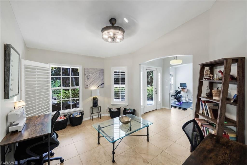 Bright room featuring tile flooring, multiple windows with white plantation shutters, a contemporary ceiling light fixture, and an arched doorway