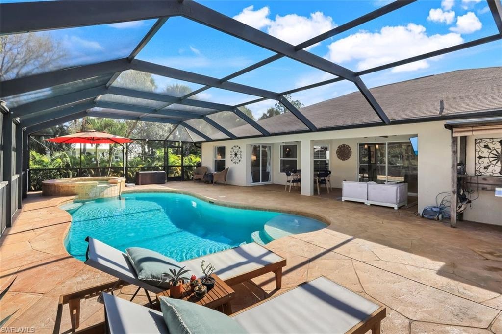 Screened outdoor living area featuring a freeform pool with integrated spa, expansive stamped concrete decking, and direct access to the interior