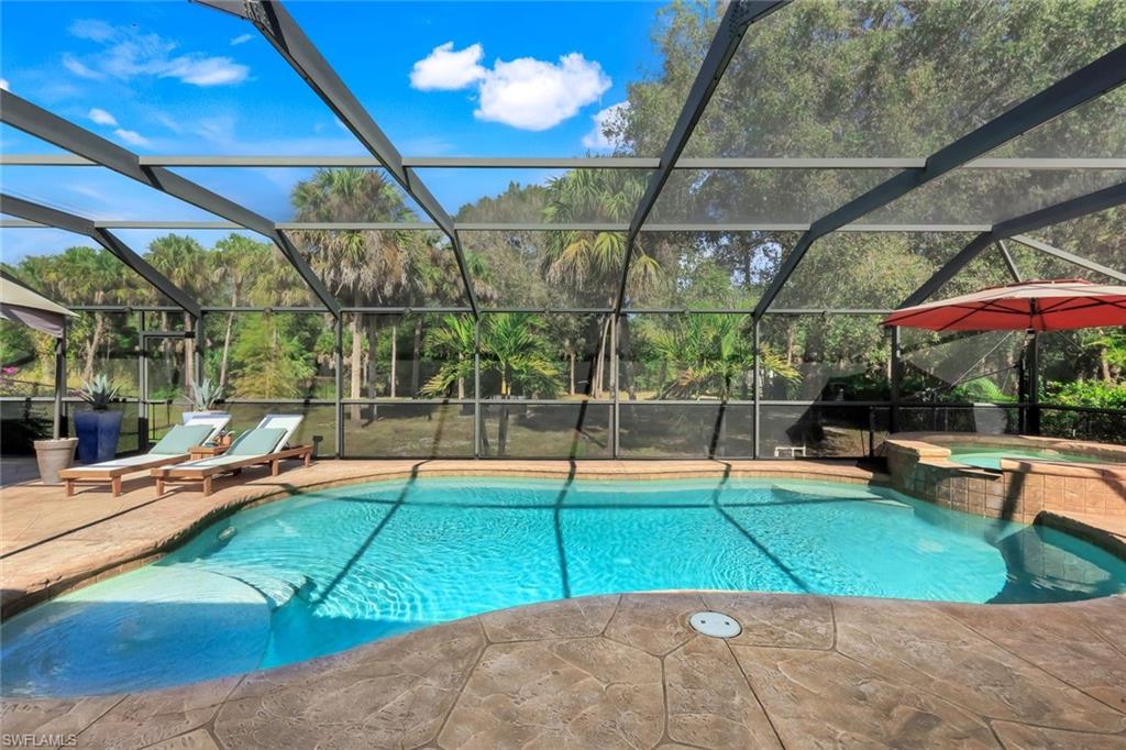 Screened lanai w/ swimming pool area featuring heated pool, integrated spa with waterfall, stamped concrete decking, and lush natural landscaping beyond the enclosure