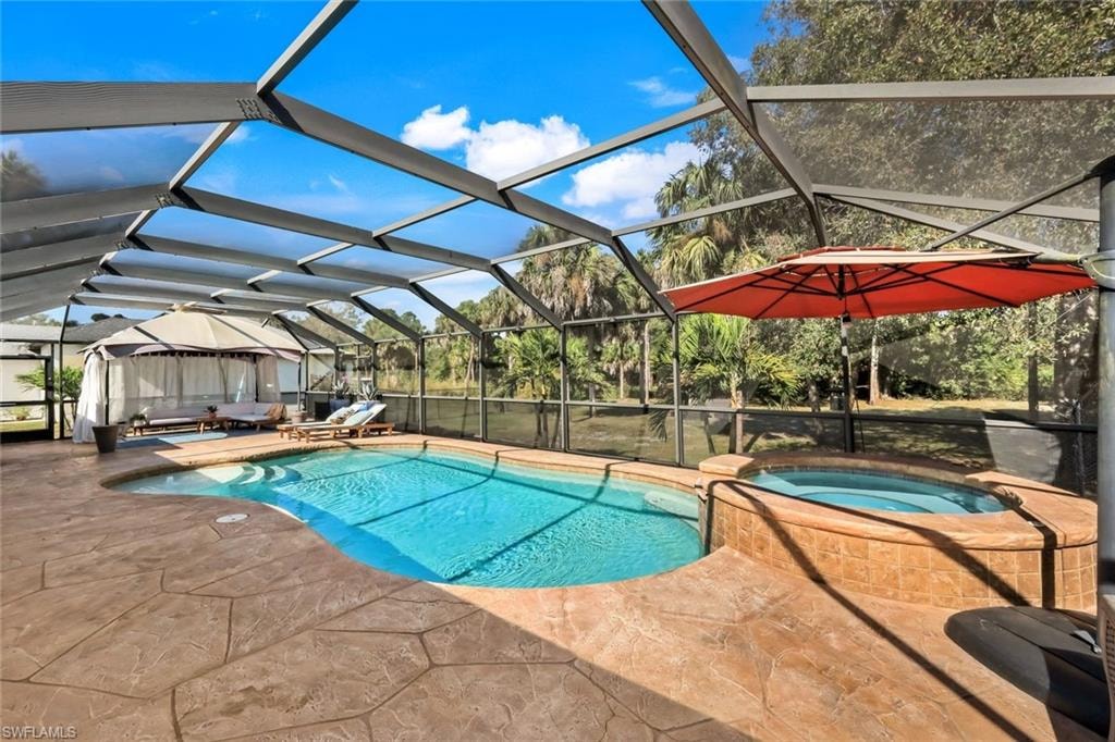 Screened lanai almost 2k sq ft featuring a freeform heated swimming pool, integrated hot tub with stone-look tile surround, and extensive stamped concrete decking