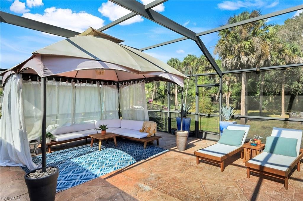Screened enclosure featuring a stamped concrete patio, a covered outdoor lounge area, mature landscaping, and a tropical tree-lined perimeter