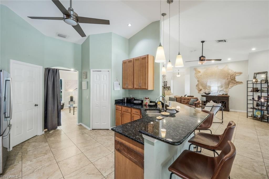 Kitchen featuring granite countertops, wood cabinetry, stainless steel sink, pendant lighting, and tile flooring