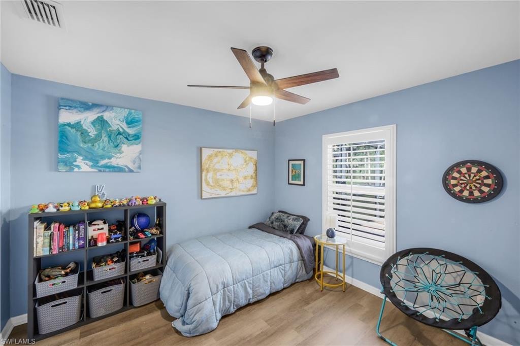 Room featuring wood-finish flooring, a ceiling fan with integrated lighting, and a window with white plantation shutters