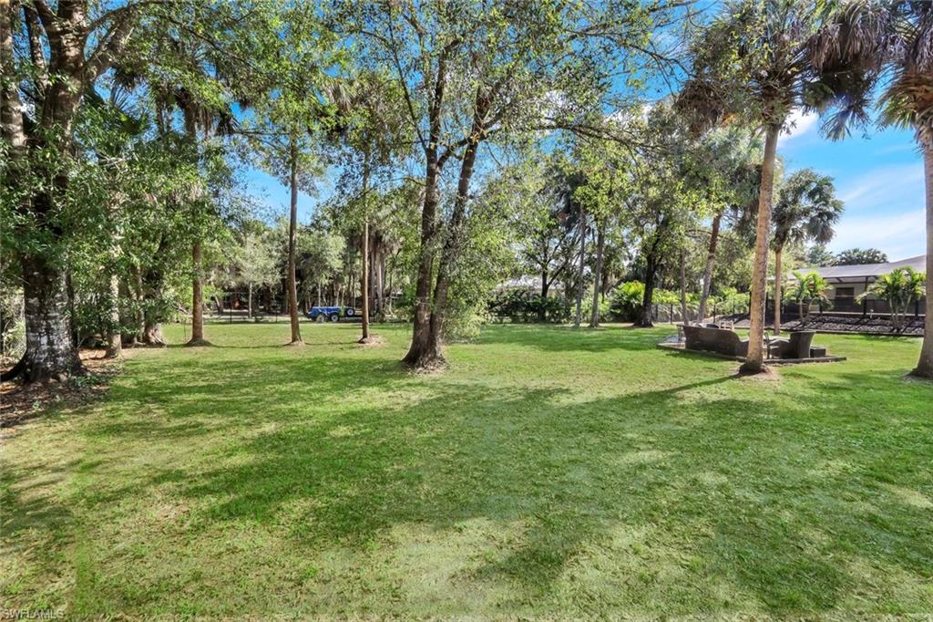 Expansive backyard featuring a manicured lawn, mature trees, and a dedicated outdoor patio area with built-in hardscaping