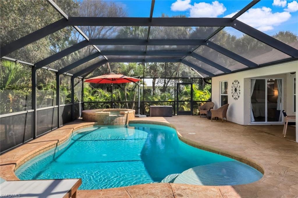 Screened-in outdoor living space featuring a freeform swimming pool, an integrated spa with stone-finish surround, and a spacious concrete patio