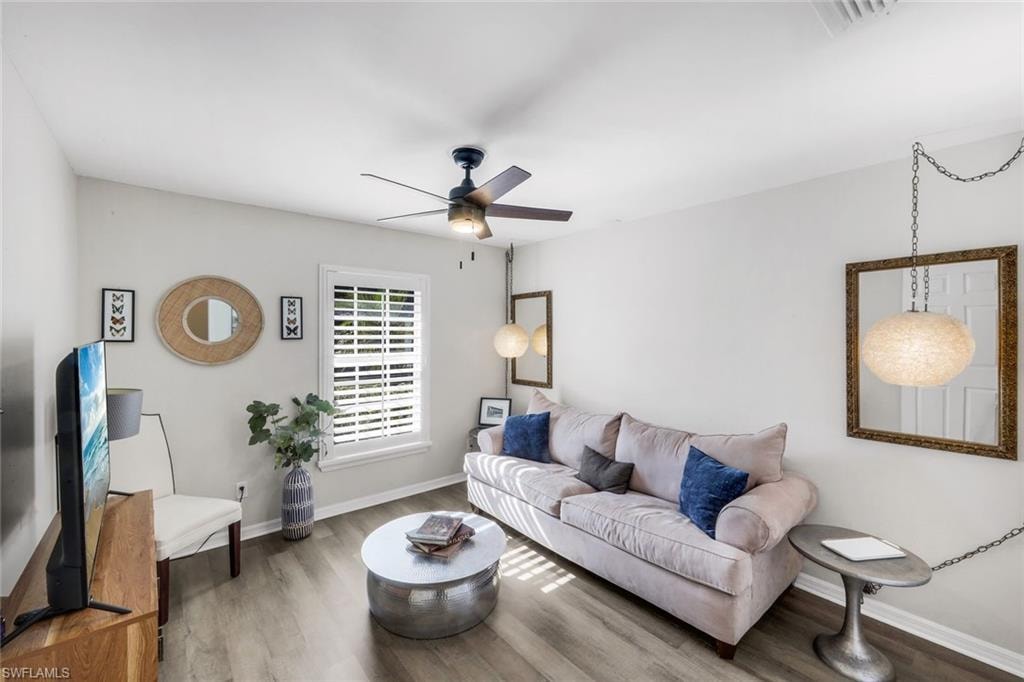Living area featuring wood-finish flooring, a ceiling fan with integrated lighting, and a window with white plantation shutters