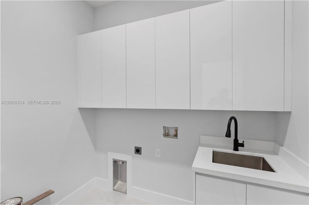 Utility room featuring a built-in sink with a matte black faucet, white upper and lower cabinetry, and a light-toned countertop