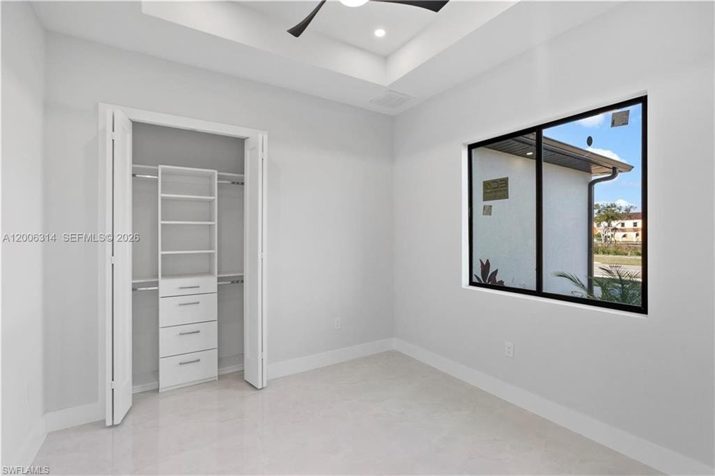 Spacious room featuring a tray ceiling with recessed lighting, large black-framed window, and a built-in closet organization system with shelving and drawers