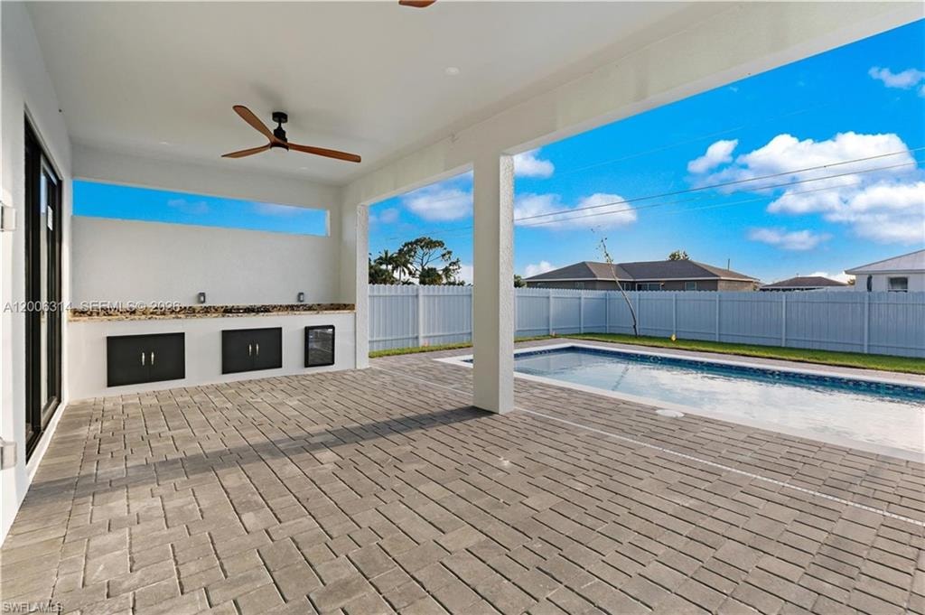 Expansive covered patio featuring a wood-finish ceiling fan, built-in counter with cabinetry, and a rectangular swimming pool with paved decking