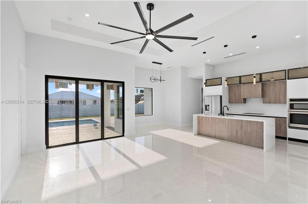 Open-concept living space featuring high ceilings with a modern ceiling fan, large format tile flooring, and multi-panel sliding glass doors opening to an outdoor patio with a swimming pool