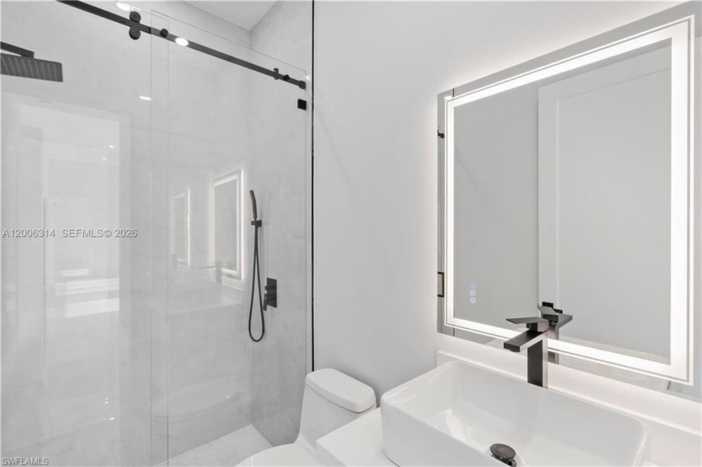 White ceramic rectangular vessel sink with a matte black faucet, illuminated mirror, and a frameless glass shower enclosure featuring a matte black rain shower head and handheld sprayer