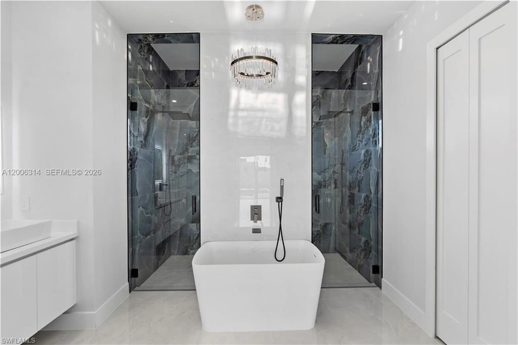 Freestanding soaking tub with a floor-mounted faucet, flanked by two walk-in showers featuring glass enclosures and dark stone-look tile