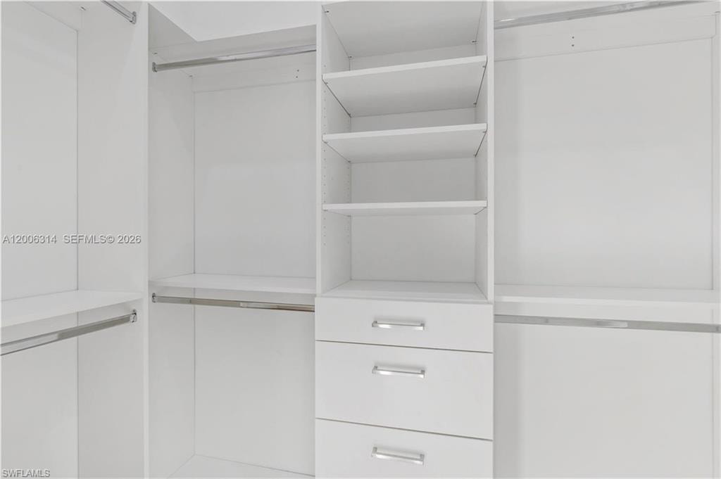 Custom closet system featuring white cabinetry, integrated shelving, three pull-out drawers with chrome hardware, and multiple chrome hanging rods