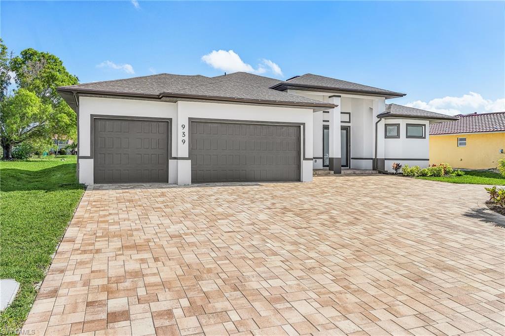 Contemporary exterior featuring a paver driveway, two-car garage, white stucco facade with dark trim, and a covered entry