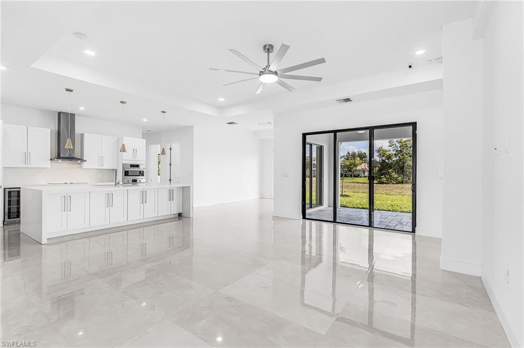 Open-concept kitchen and living area featuring polished tile flooring, a large island with integrated storage, white cabinetry, stainless steel appliances, and a beverage refrigerator