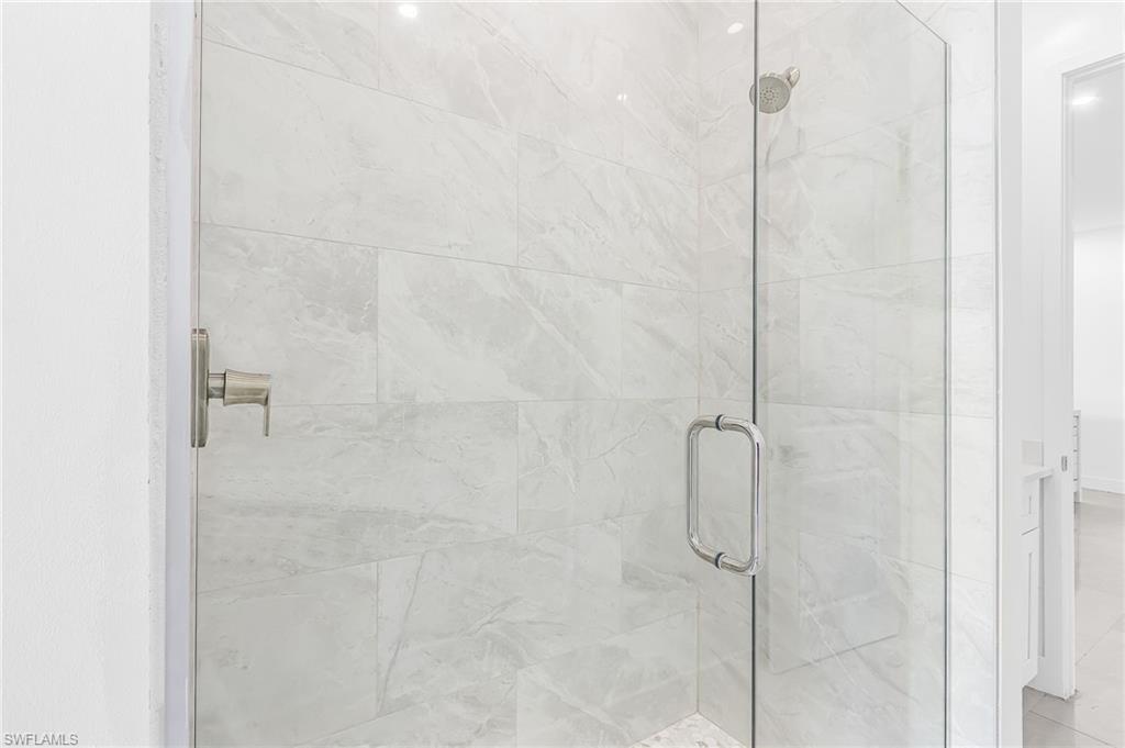 Glass-enclosed shower featuring large format tile with subtle veining, a brushed nickel shower control, and a rain shower head