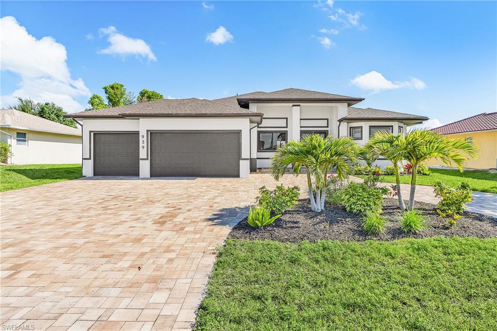 Contemporary single-story residence featuring a paved driveway, two-car garage, manicured lawn, and tropical landscaping