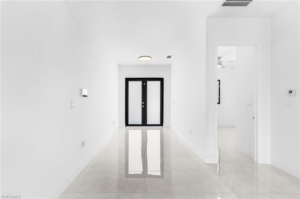 Entryway featuring a black double-door with frosted glass inserts, polished tile flooring, white baseboards, and a flush-mount ceiling light