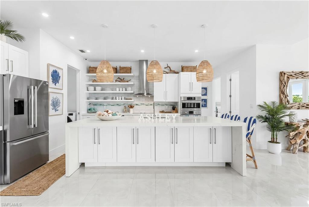 Spacious kitchen featuring a large central island with seating, stainless steel appliances, white cabinetry, and open shelving