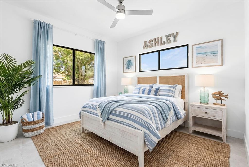 Bright room featuring large windows, a ceiling fan, light tile flooring, a woven area rug, and a bed with a rattan headboard