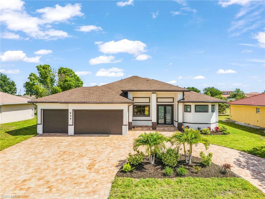 Contemporary stucco exterior featuring a brown shingle roof, paver driveway, two-car garage, and double entry doors