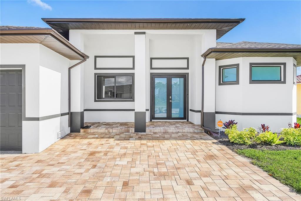 Contemporary exterior featuring a paver driveway, double-door entry, a two-tone exterior finish, and integrated landscaping