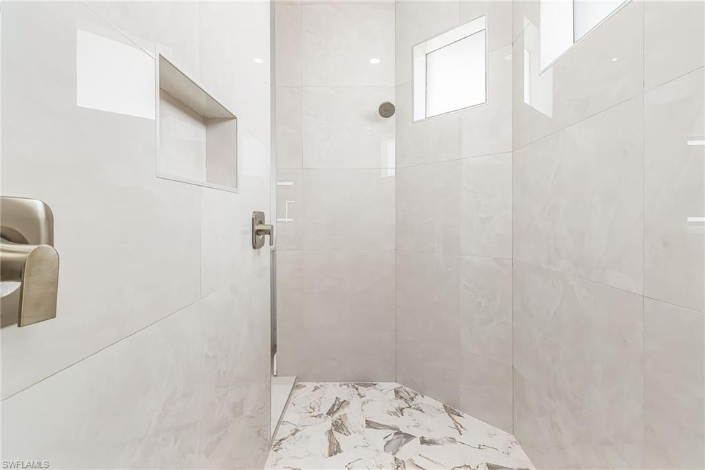 Shower stall with large format white tile walls, a built-in shower niche, and a contrasting patterned tile floor