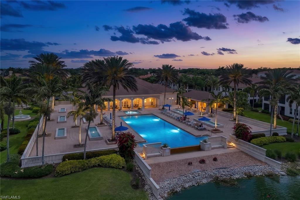 Expansive swimming pool and spa area featuring a paver deck, mature palm trees, decorative water features, and a waterside promenade