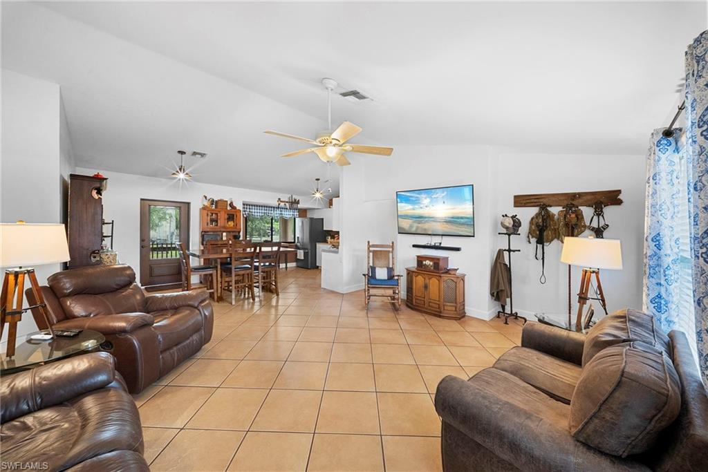 Open-concept living area with neutral tile flooring, vaulted ceilings, and a ceiling fan