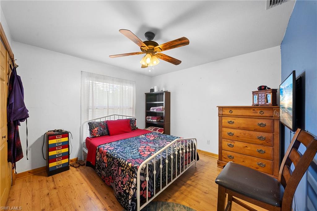 Bright room featuring light wood-finish flooring, a ceiling fan with integrated lighting, and a large window with blinds