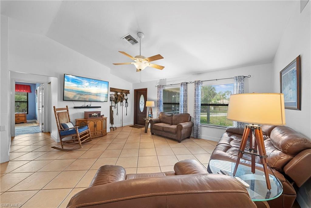Spacious living area featuring vaulted ceilings, light-toned tile flooring, and multiple windows with blinds