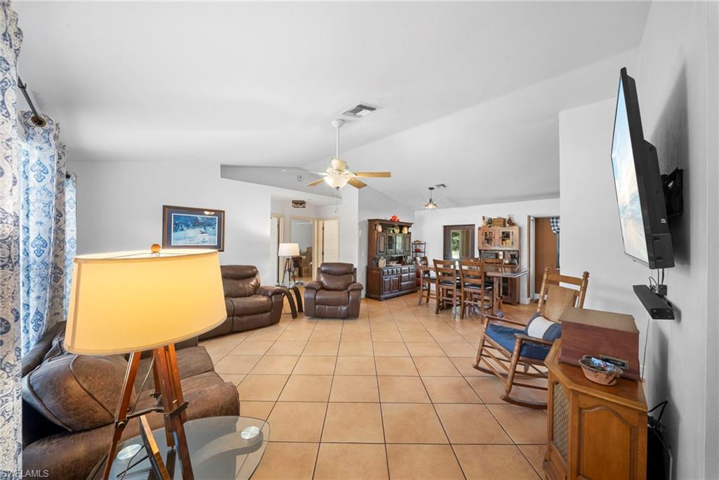 Spacious interior featuring tile flooring throughout, vaulted ceilings, a ceiling fan, and an open layout connecting living and dining areas