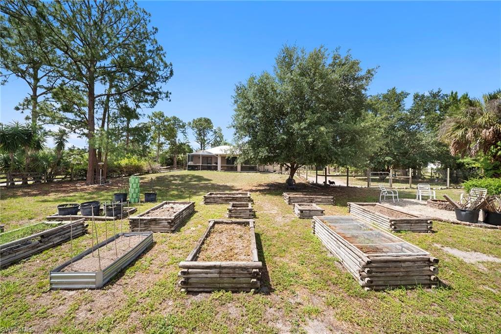 Expansive grounds featuring multiple raised garden beds, mature trees, and a screened patio structure