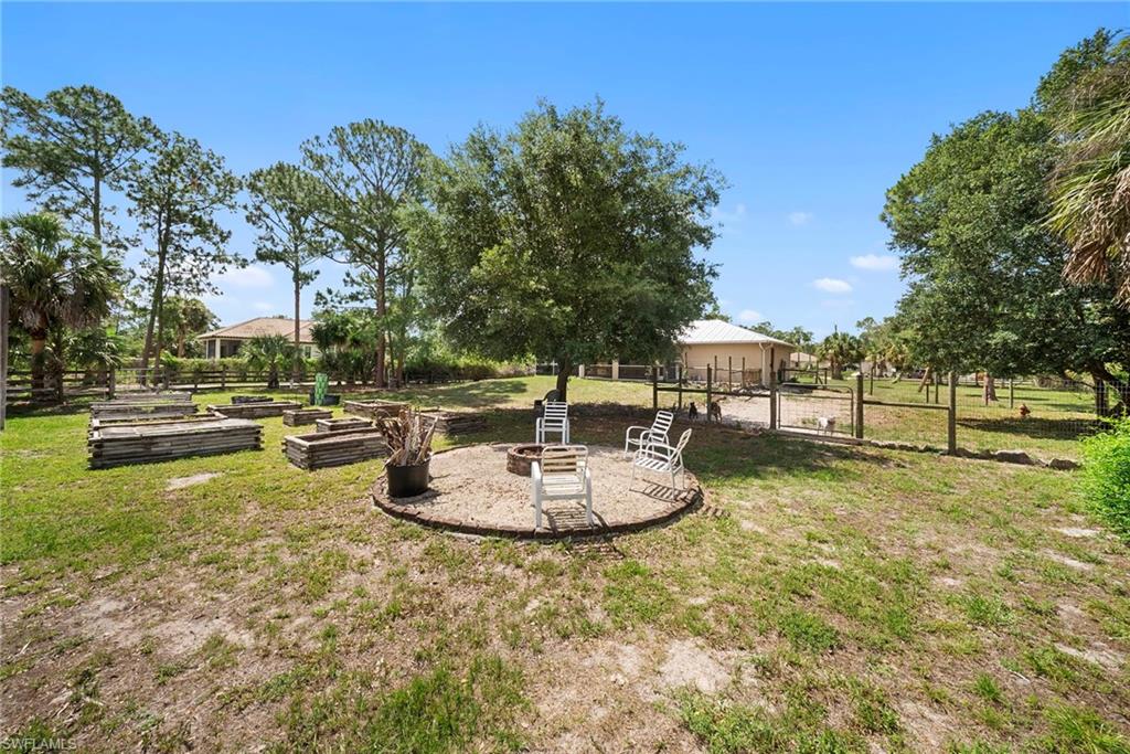 Expansive outdoor area featuring a circular fire pit area with paver edging, mature trees, and multiple raised garden beds
