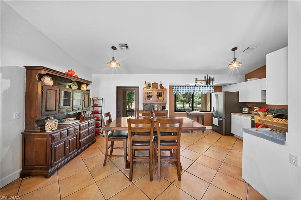 Open-concept dining and kitchen area featuring tile flooring, white shaker cabinetry, stainless steel appliances, and a window overlooking exterior landscaping