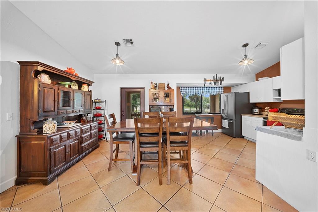 Open-concept living area featuring a kitchen with white cabinetry and dark appliances, a dining space with tiled flooring, and a large window overlooking exterior scenery