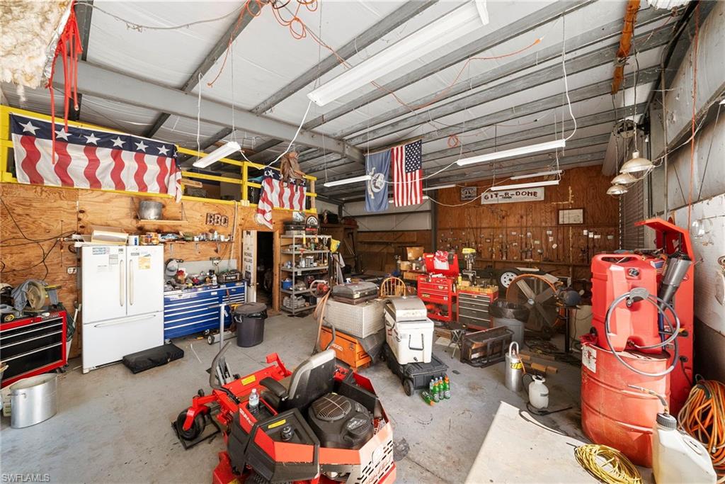 Spacious utility building featuring a high ceiling, exposed structural beams, a mezzanine level, fluorescent lighting, and extensive wall-mounted storage options