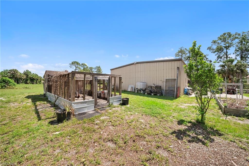 Expansive outdoor space featuring a large metal-sided outbuilding, a wood-framed structure with a metal base, and raised garden beds