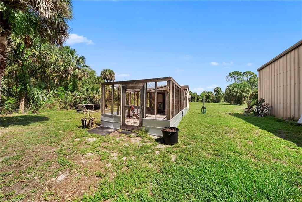 Expansive outdoor area featuring a wooden framed structure, a metal-sided building, mature palm trees, and a substantial grass lawn