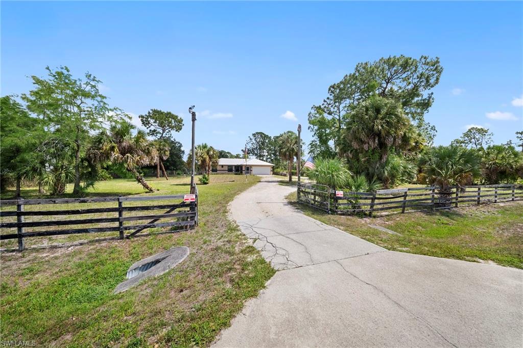 Gated entry featuring a paved driveway, a split-rail fence, and mature landscaping