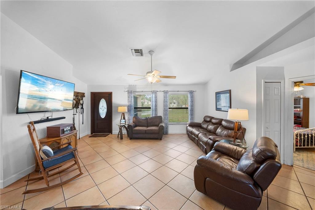 Open-concept living space featuring high vaulted ceilings, light-toned tile flooring, and a ceiling fan with integrated lighting
