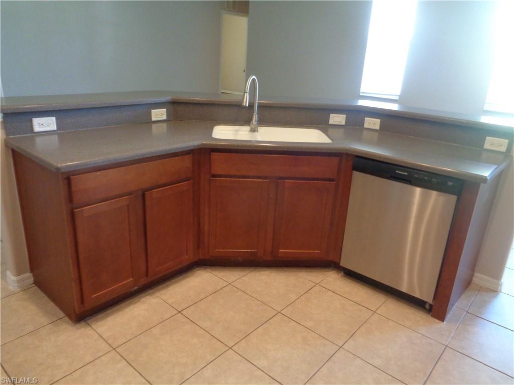 Kitchen island with stainless steel dishwasher, light brown cabinetry, Corian countertops, and tile flooring