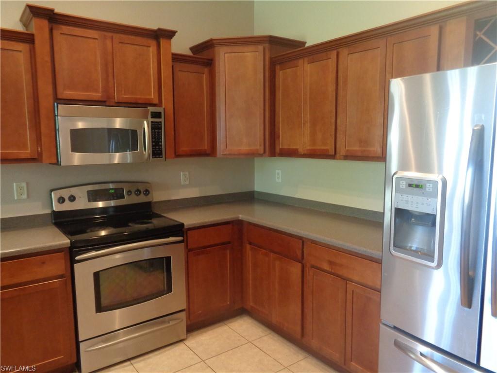 Kitchen with stainless steel appliances, light brown cabinetry, Corian countertops, and tile flooring