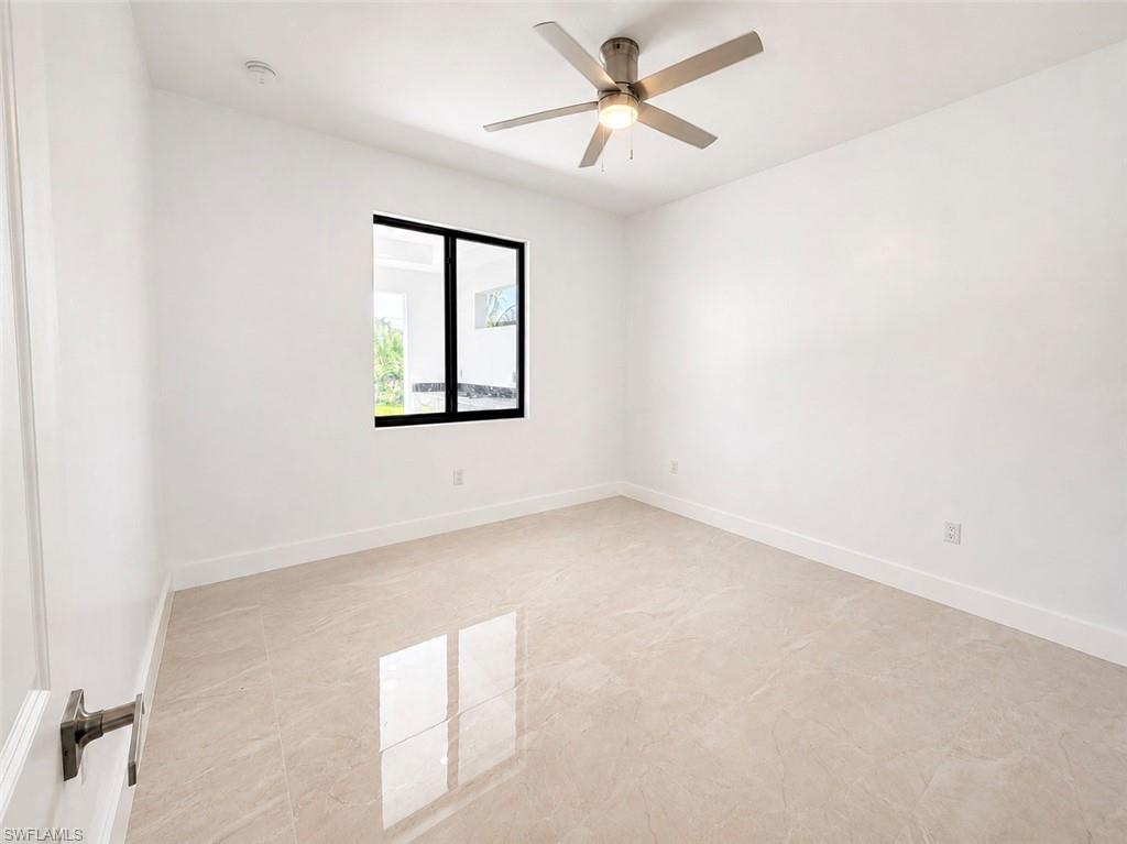 Bright interior space featuring large format rectangular tile flooring, a modern ceiling fan with integrated lighting, a black-framed window, and white baseboards